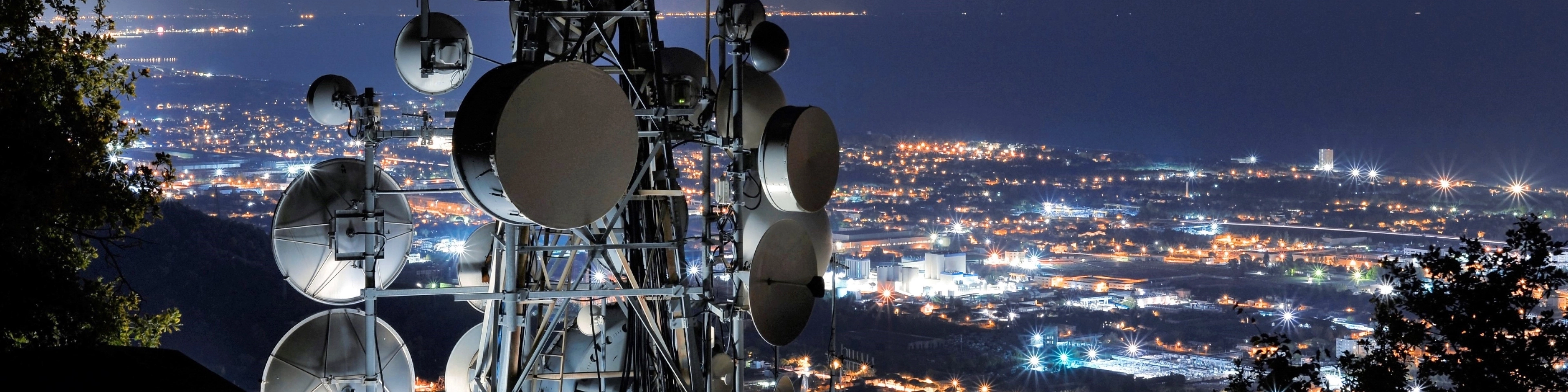 Słup z antenami telekomunikacyjnymi na tle miasta nocą