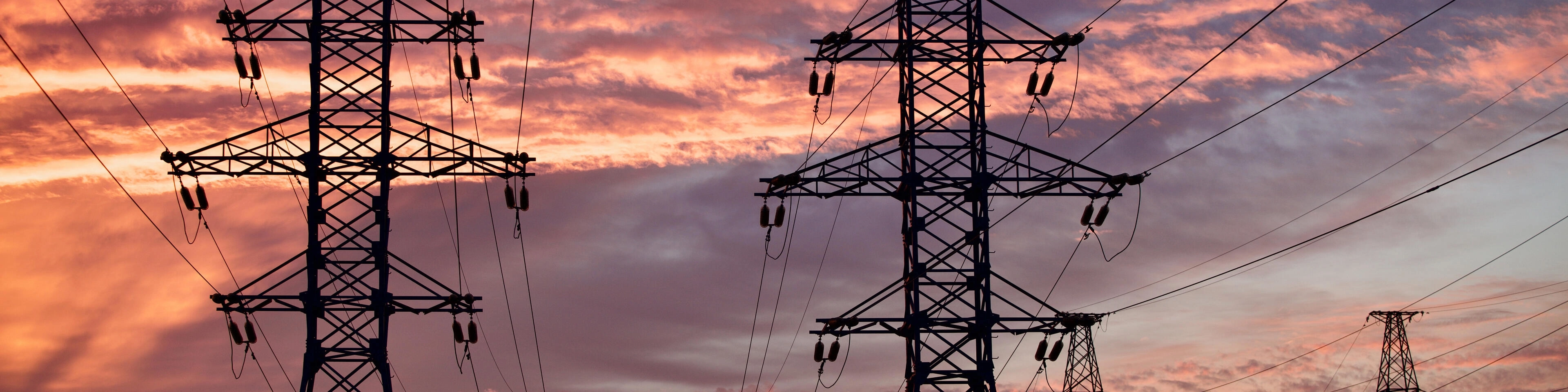 Sylwetki licznych słupów wysokiego napięcia i linii energetycznych na tle kolorowego nieba o zachodzie słońca