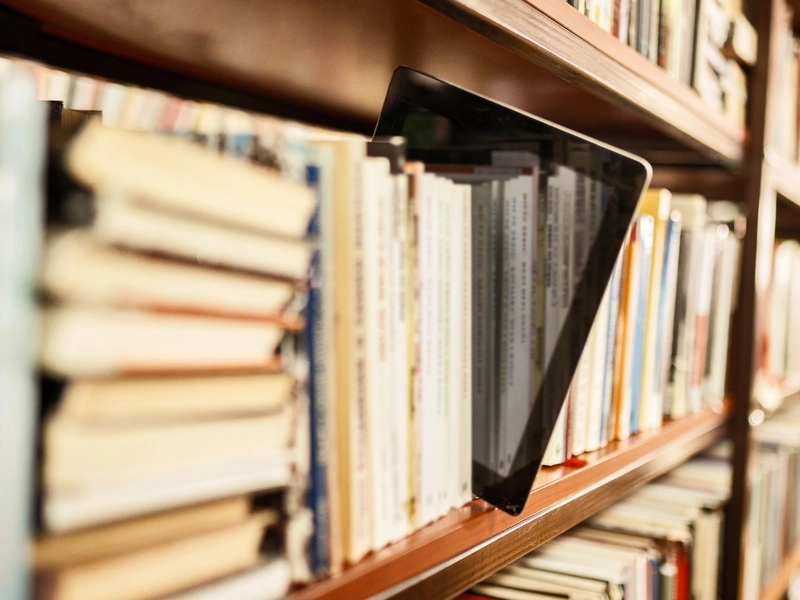 Tablet wciśnięty między ustawione na półce książki