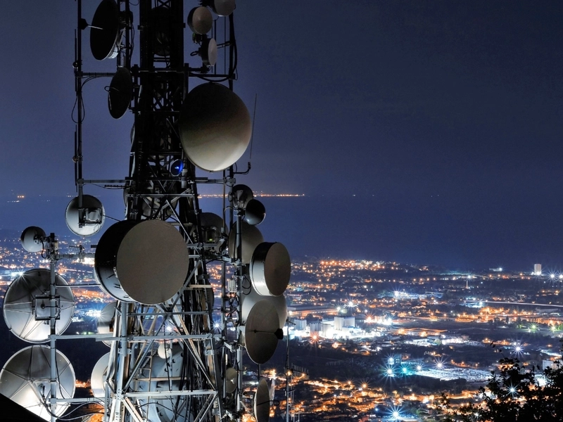 Słup z antenami telekomunikacyjnymi na tle miasta nocą