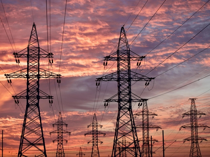 Sylwetki licznych słupów wysokiego napięcia i linii energetycznych na tle kolorowego nieba o zachodzie słońca